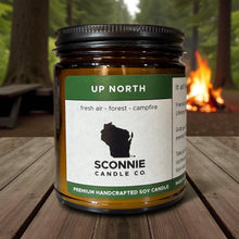 Load image into Gallery viewer, Up North Wisconsin campfire and evergreen scented soy candle burning on a rustic table.