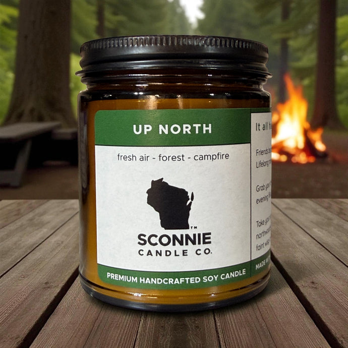Up North Wisconsin campfire and evergreen scented soy candle burning on a rustic table.